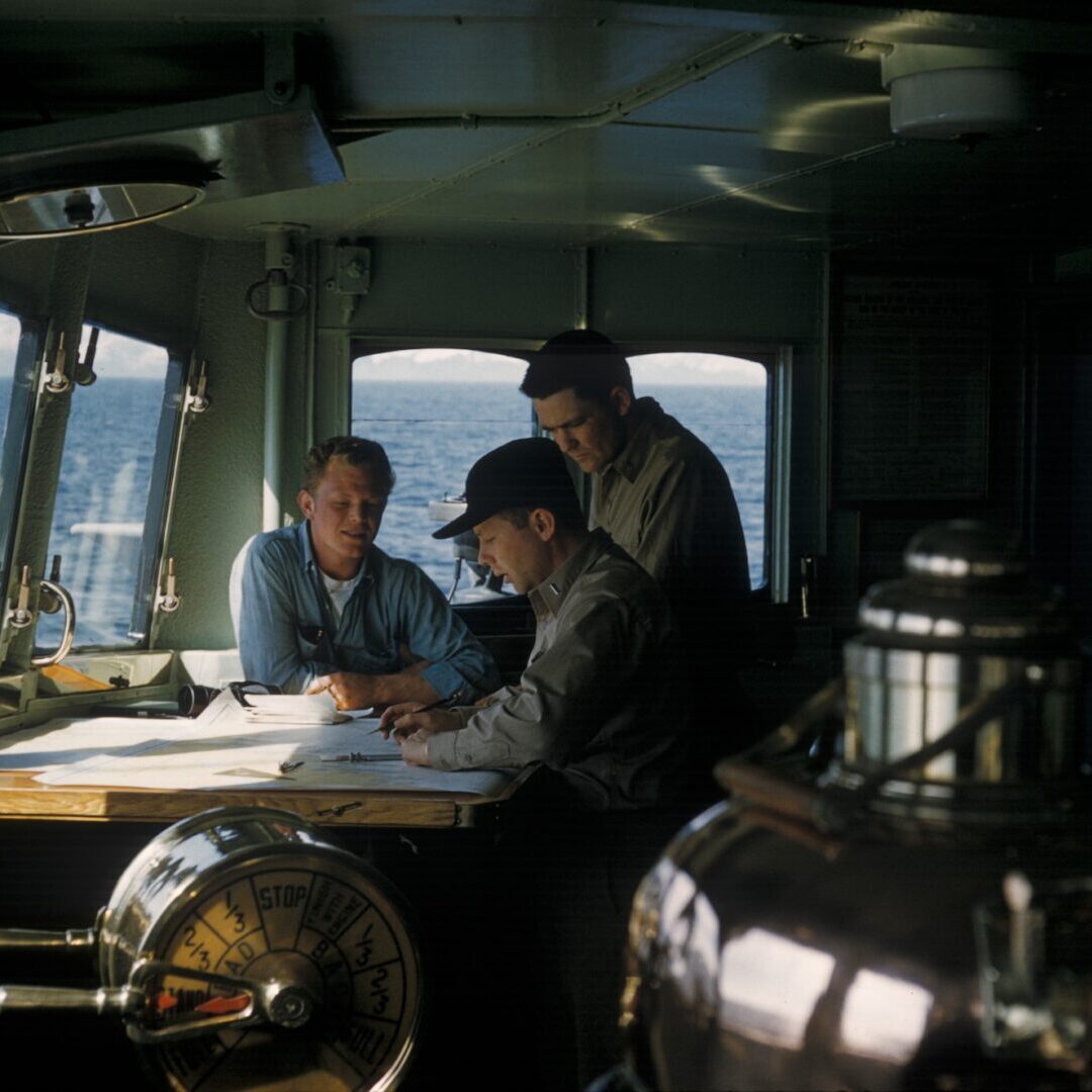 Three men sitting at a table in the middle of an ocean.